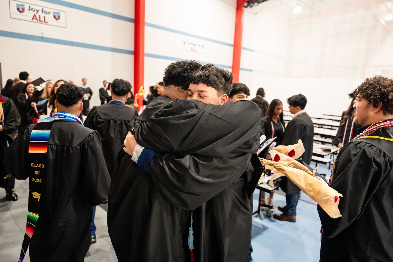 Graduates share celebratory embraces in black caps and gowns after ceremony.