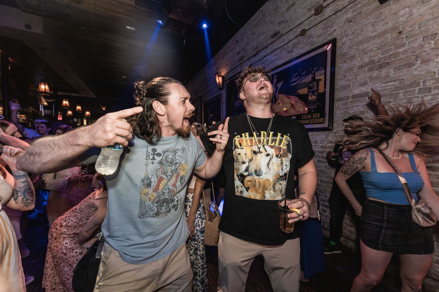 Energetic concert attendees dance and raise drinks while enjoying live music.