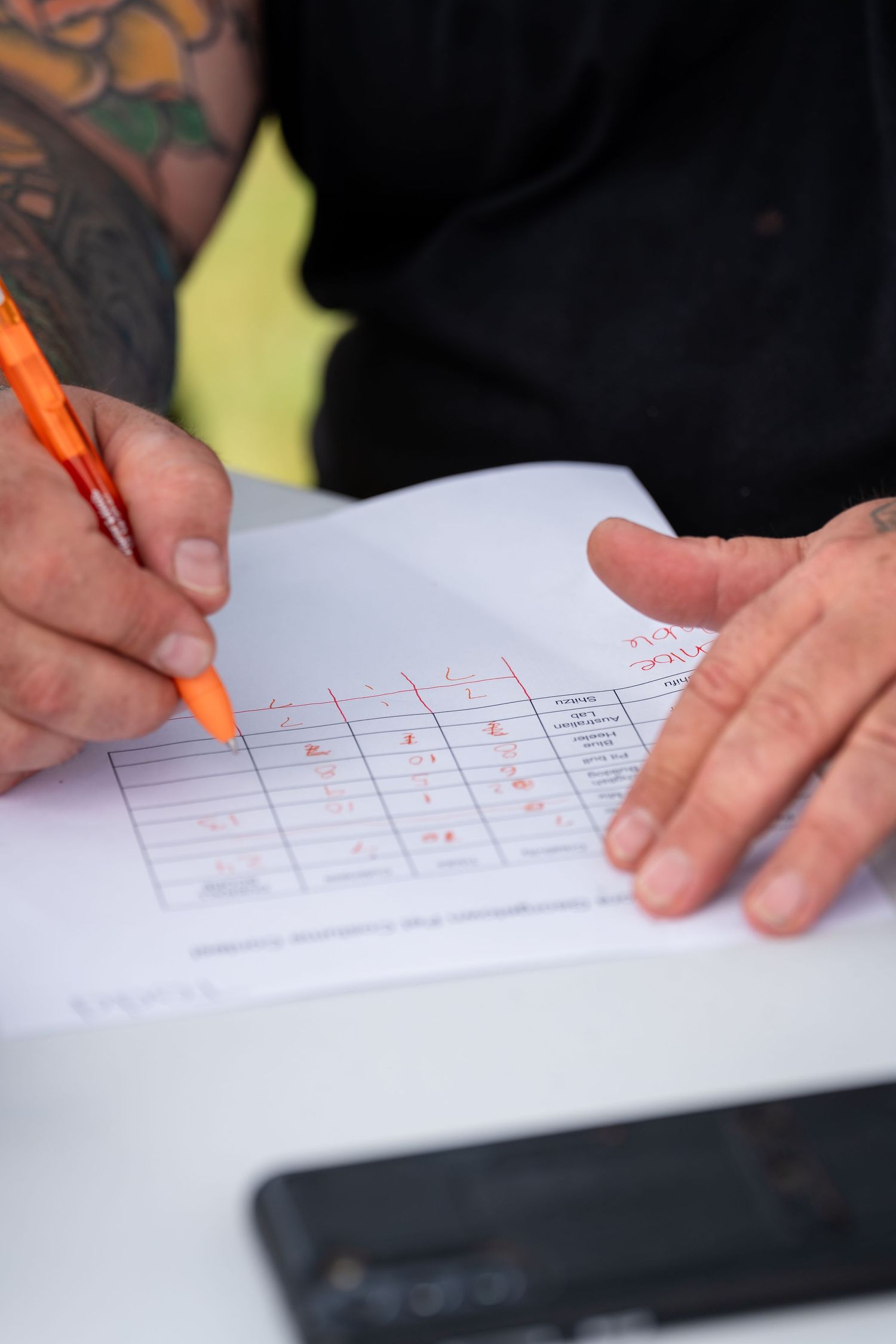 Close-up of hands writing on a form with an orange pen.