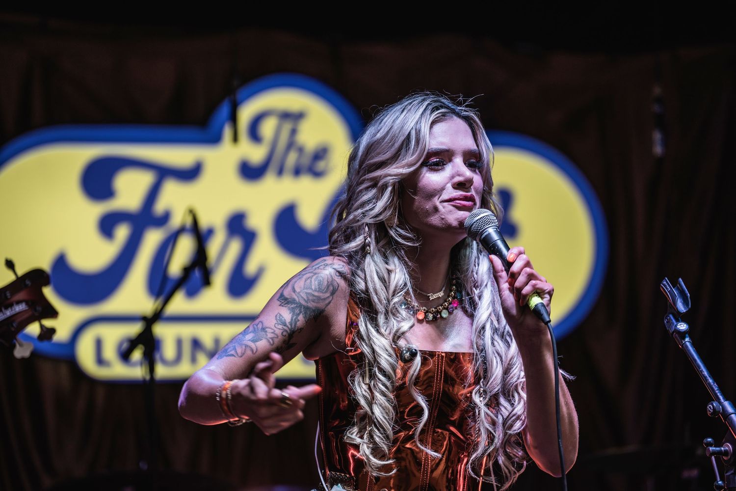 Singer performs energetically on stage with a curved blue neon sign in the background.