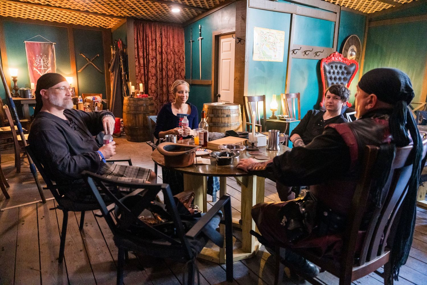 A group gathers around a wooden table in a dimly lit tavern-style setting at a medieval fair.