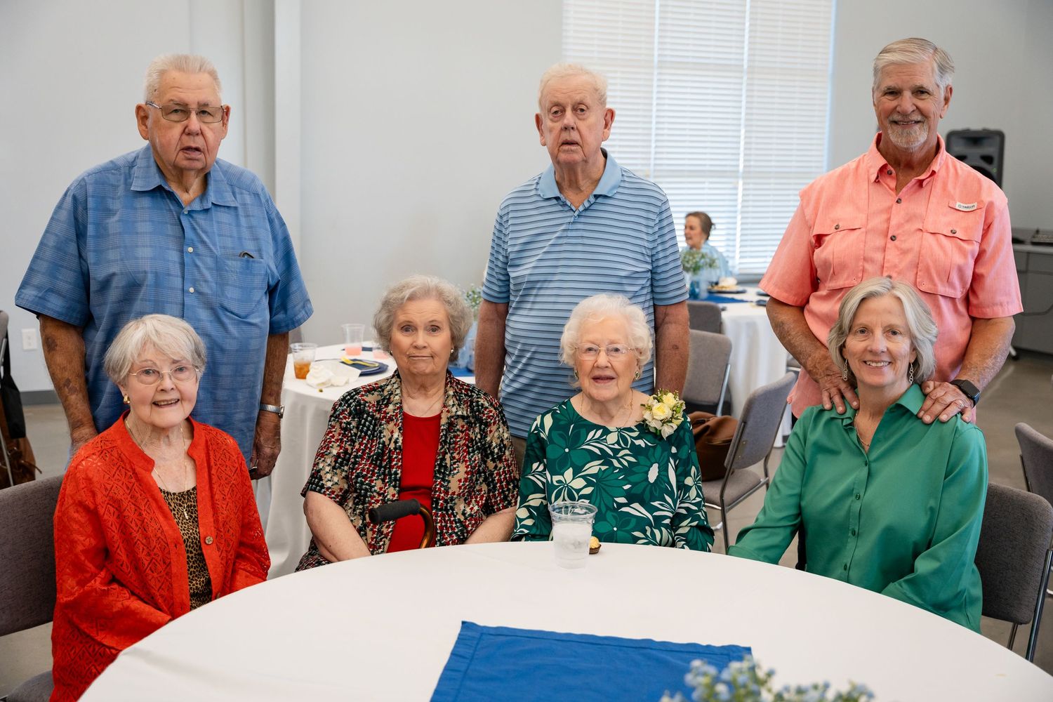A group of seniors gathered around a white table at a social event.