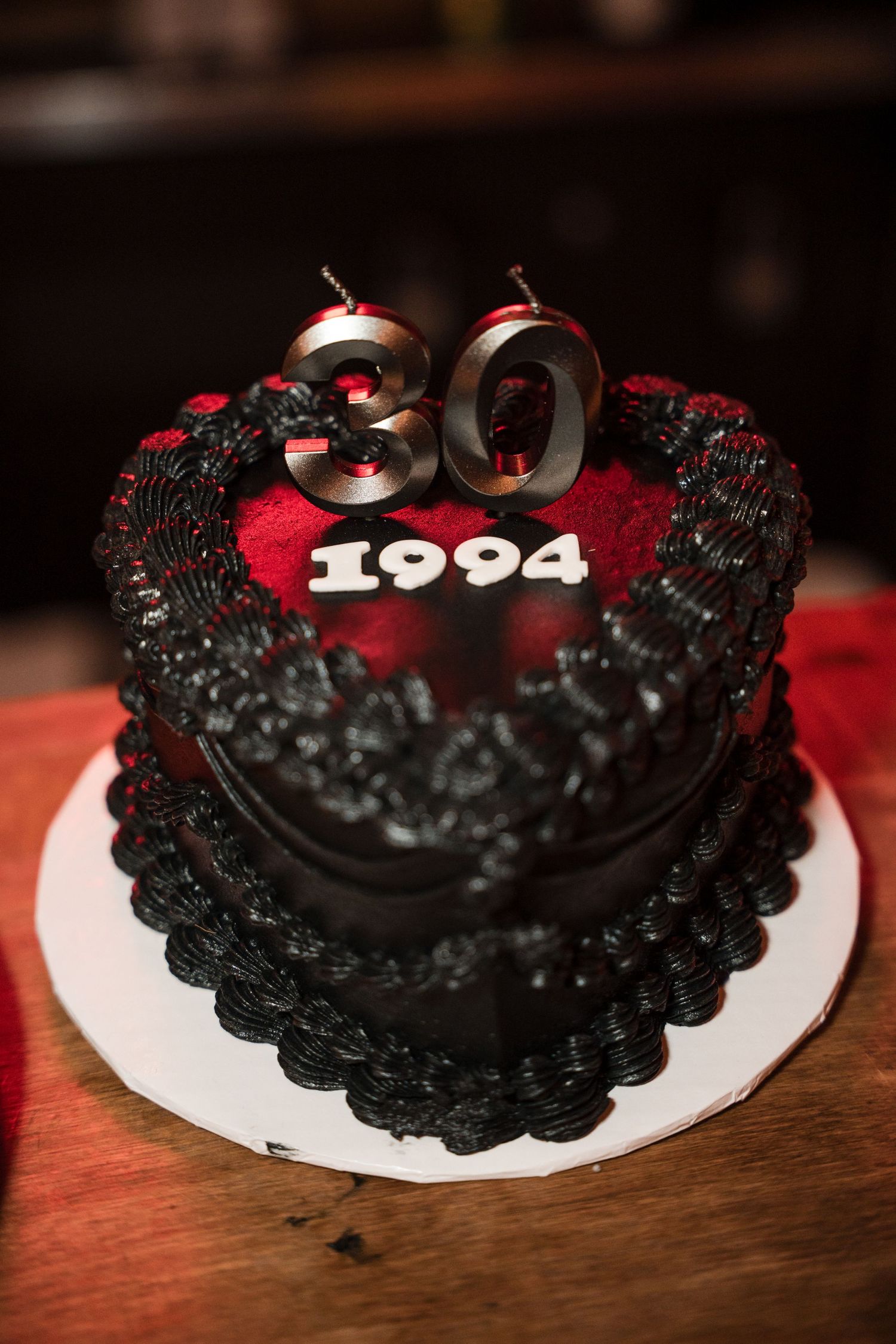 A black and red decorated birthday cake with the number 30 and year 1994 displayed on top.