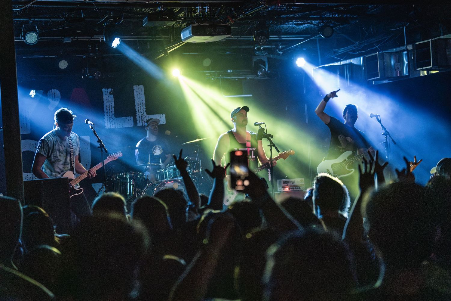 Concert crowd silhouettes with colorful stage lights and band performing live.