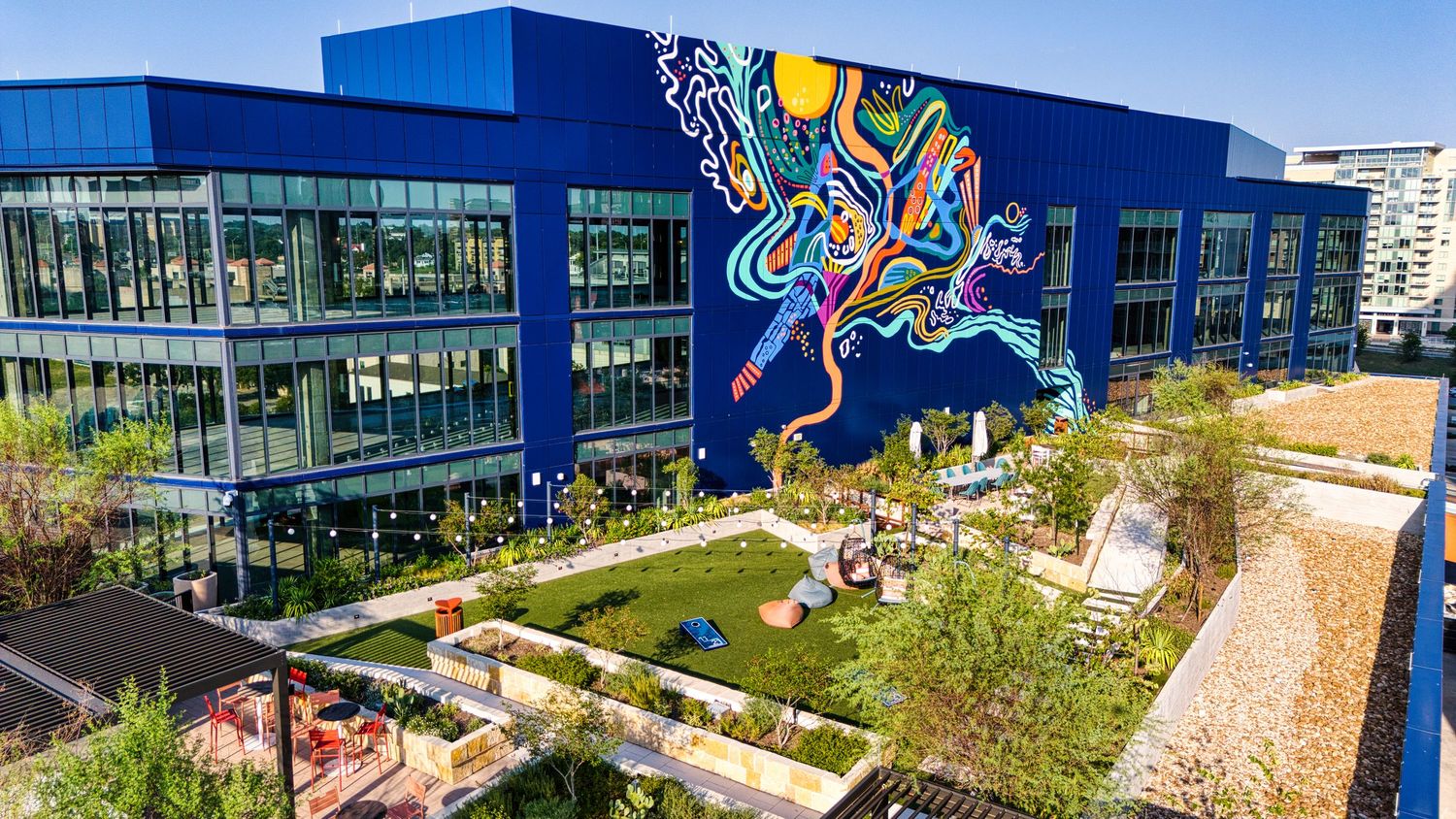 Modern apartment building with colorful mural art and landscaped courtyard garden in an urban setting.