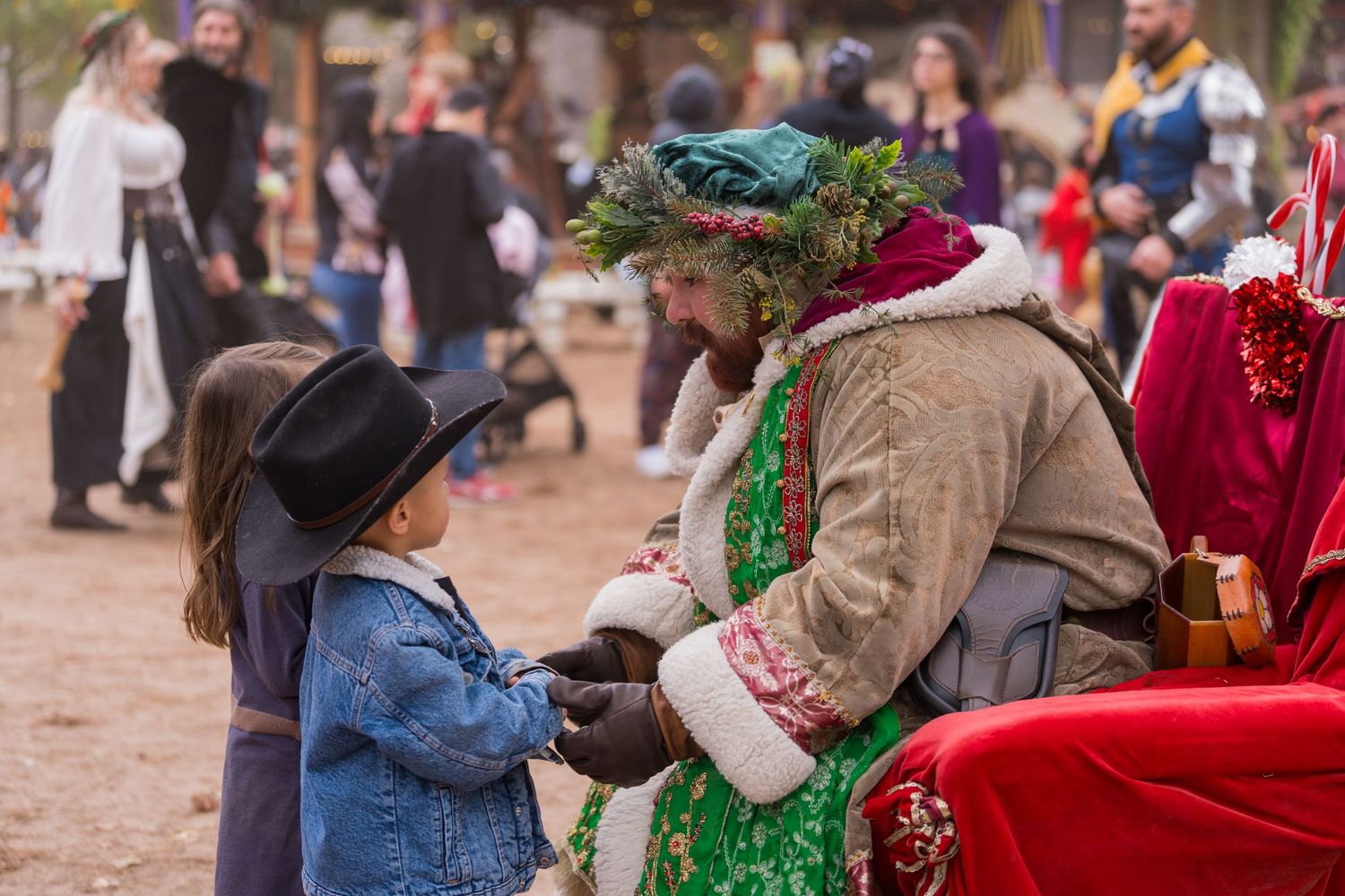 Costumed performer in medieval attire interacts with young visitor at renaissance festival.