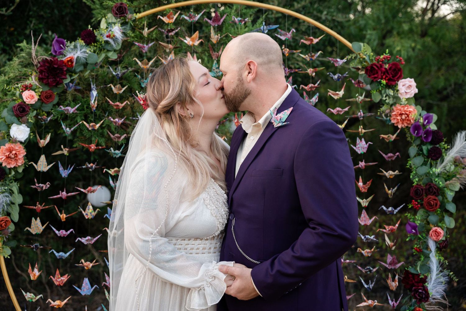 A romantic moment captured under an arch adorned with butterflies and burgundy flowers.