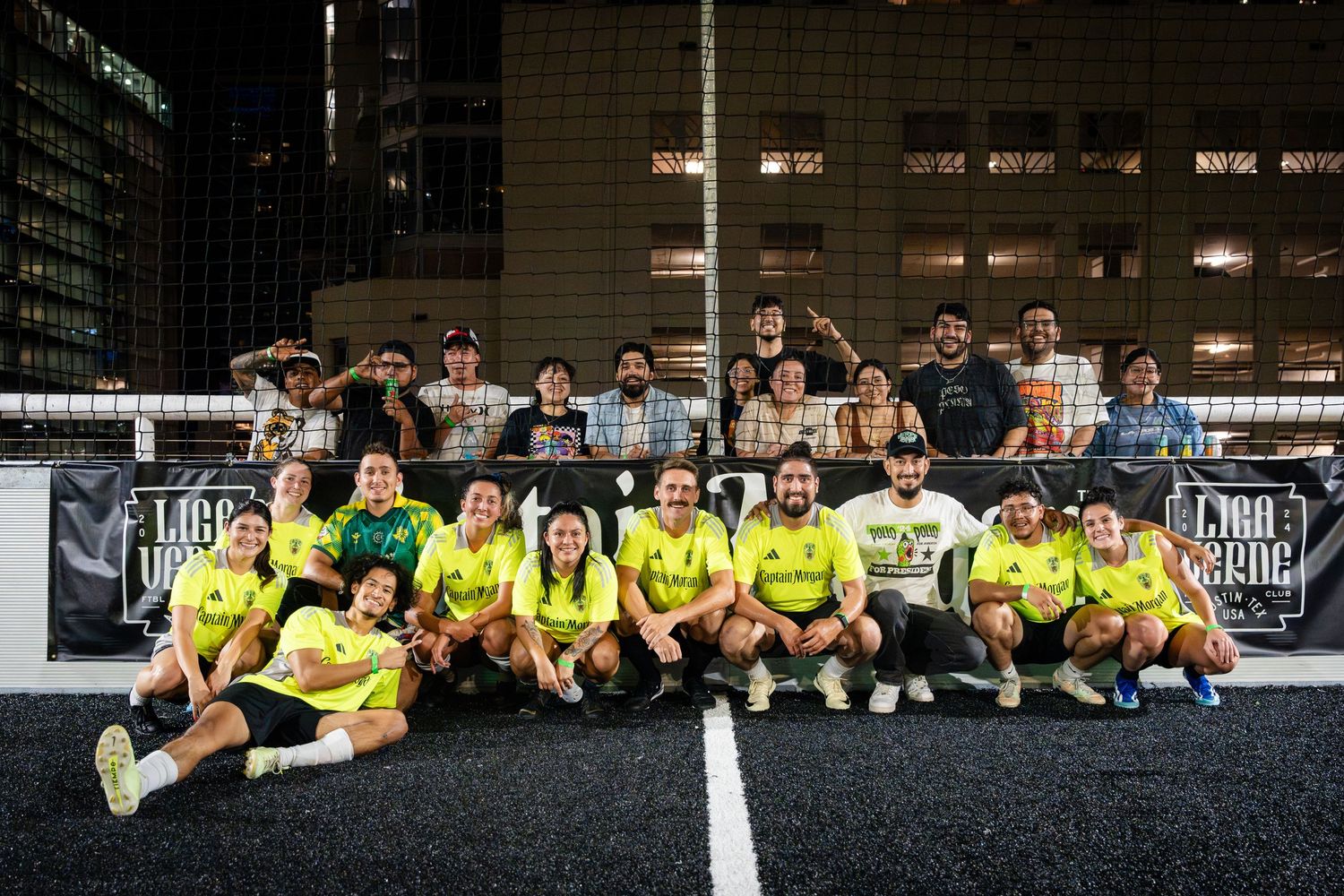 Sports team in yellow uniforms poses together on dark field at night for group photo.