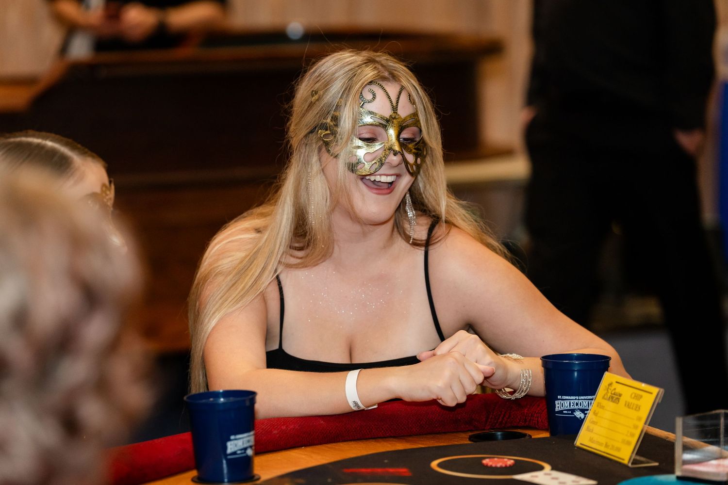 A person wearing face paint and a black top sits at a gaming table with blue cups.