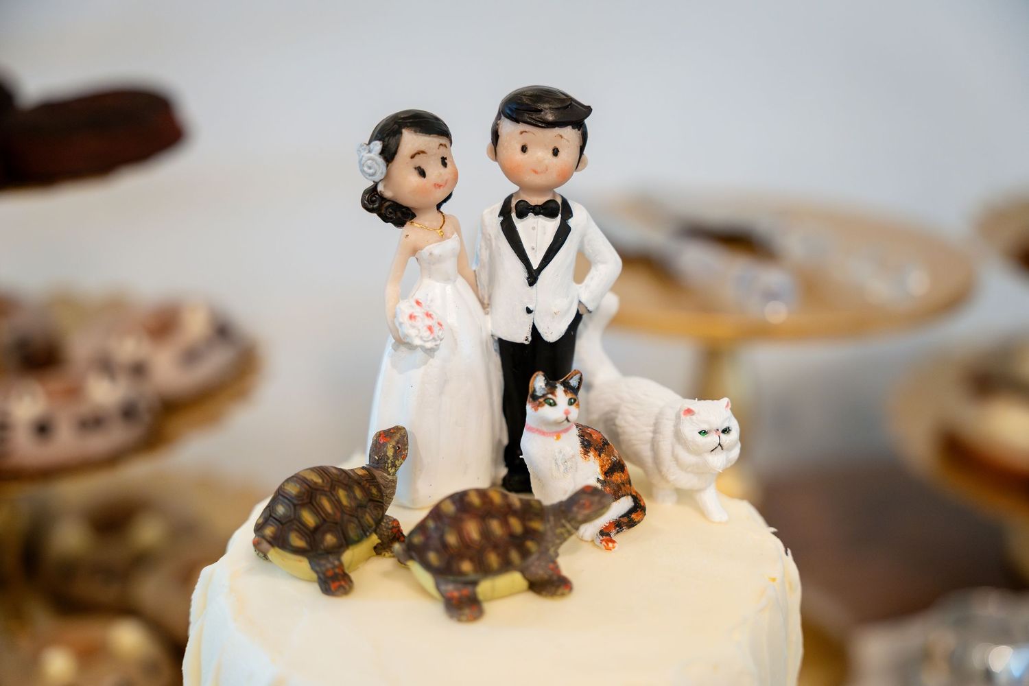 Wedding cake topper decoration with cartoon style figures and two cats - one white and one tortoiseshell.