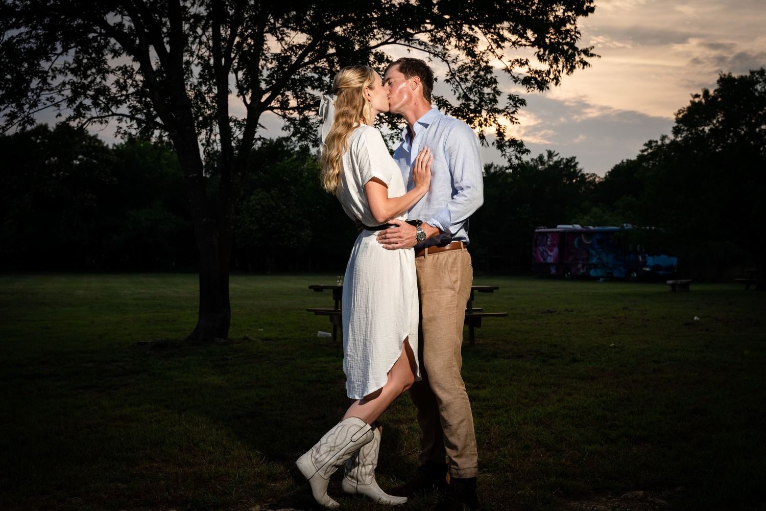 Stylishly dressed couple shares a romantic moment in a park at dusk.