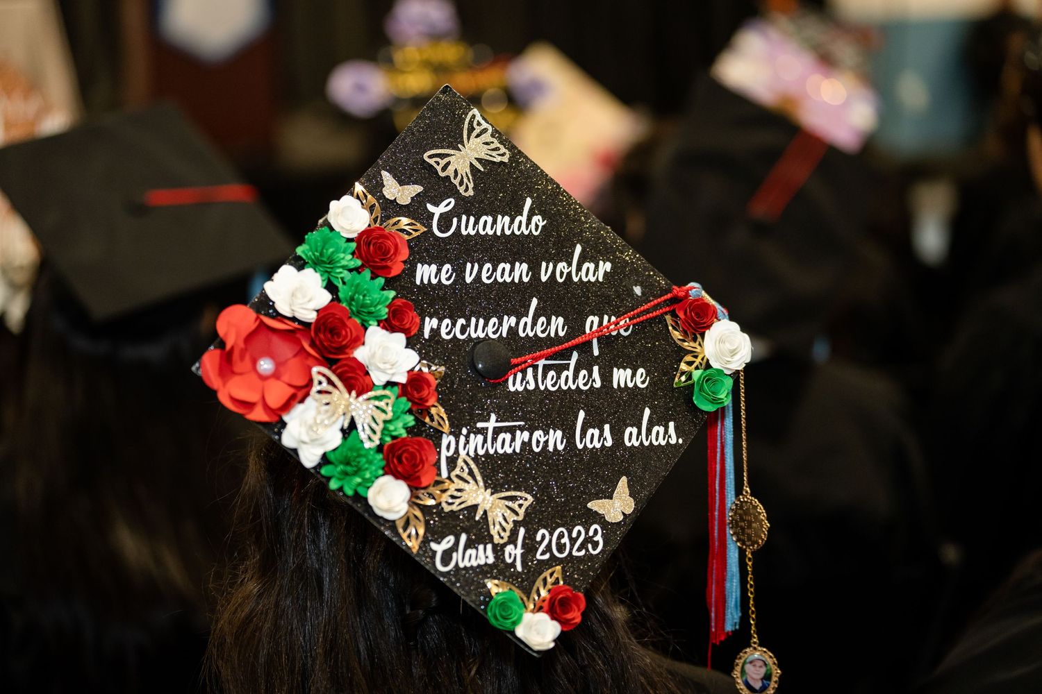 A graduation cap decorated with red and green flowers and Spanish text in metallic lettering.