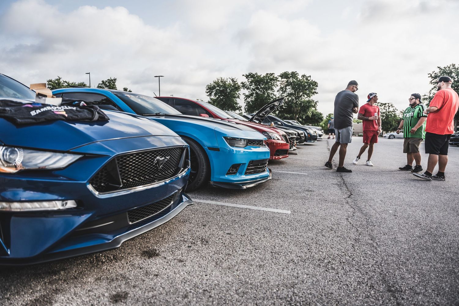 Row of performance cars parked at a car meet with gathering in background.