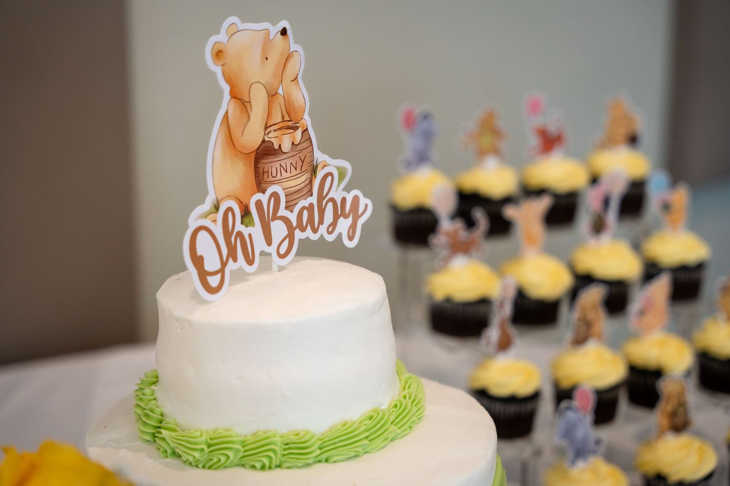 Close-up of baby shower cake with Winnie the Pooh topper and cupcakes in background.