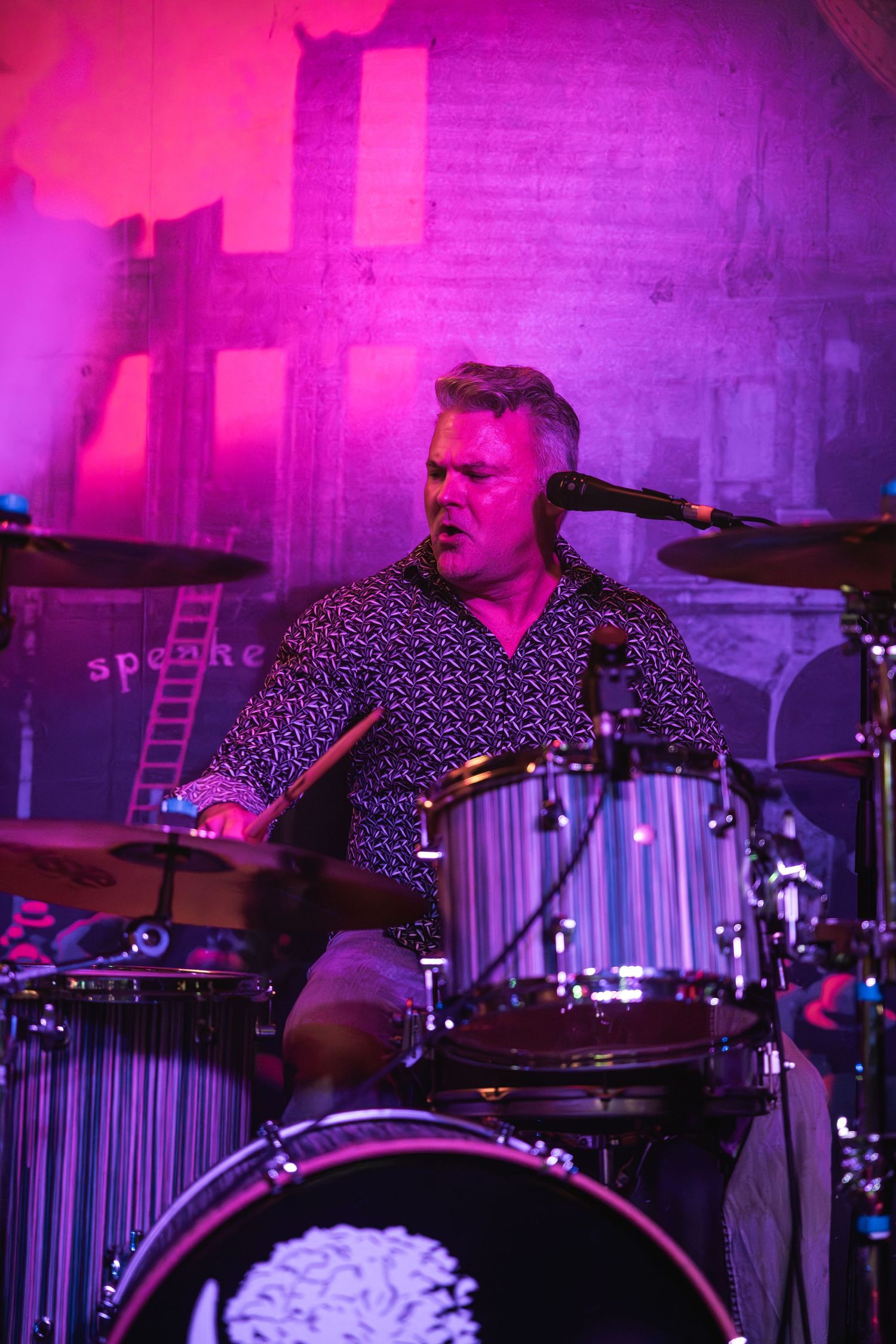 Animated drummer plays kit bathed in vibrant magenta stage lighting.