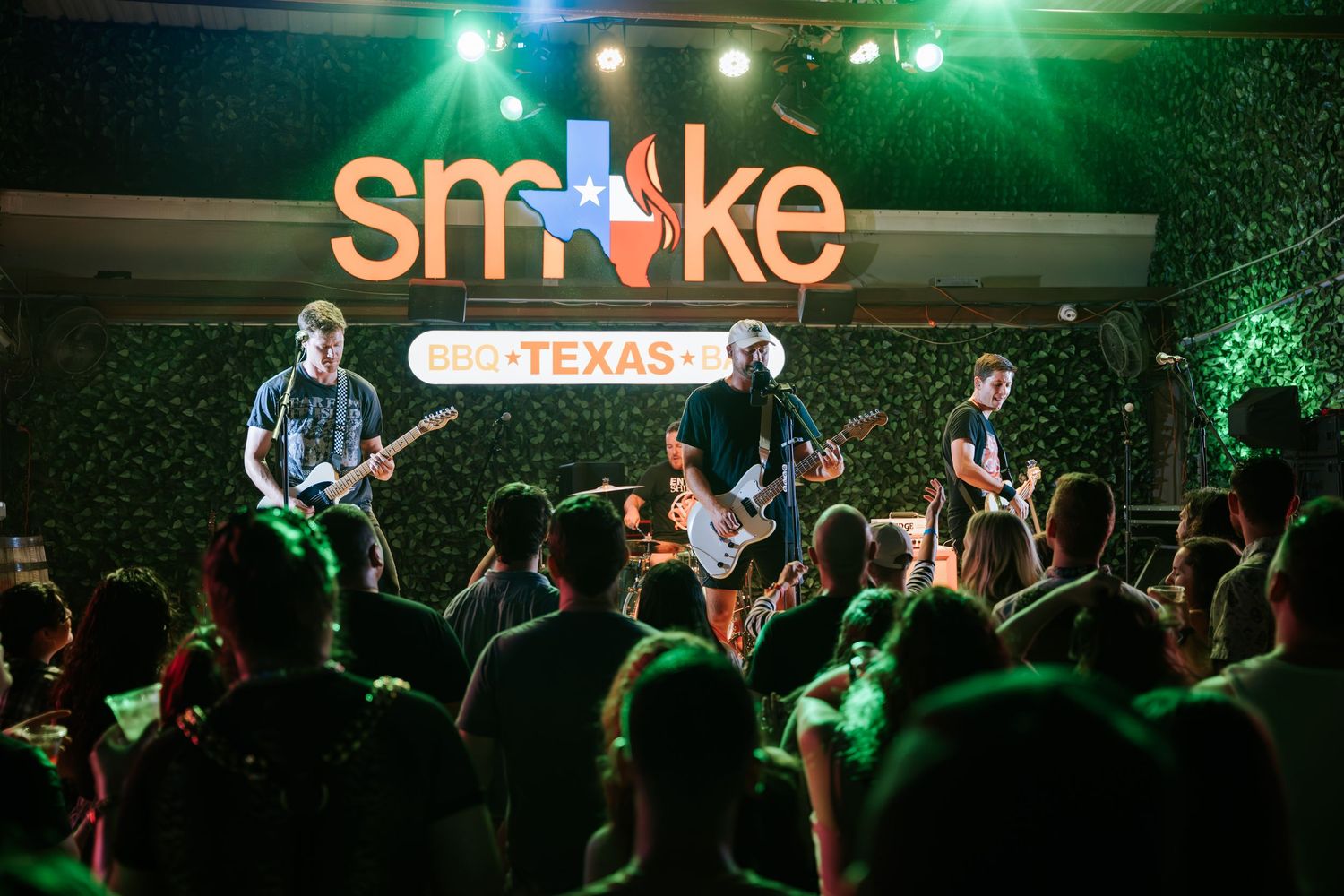 Live band playing at Smoke venue with crowd silhouettes and green stage lighting.