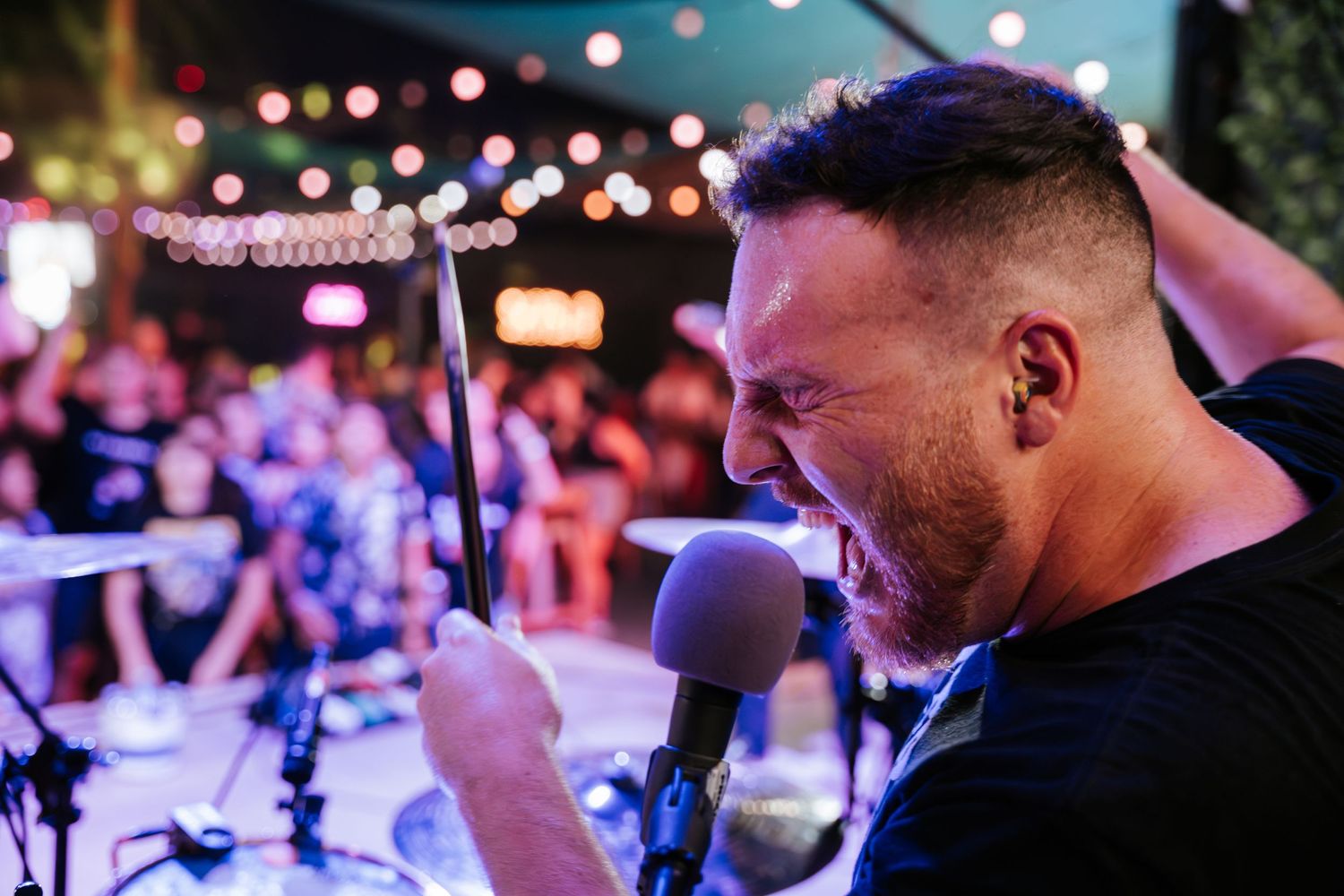 Musician delivers emotional vocal performance under ambient string lights at outdoor venue.