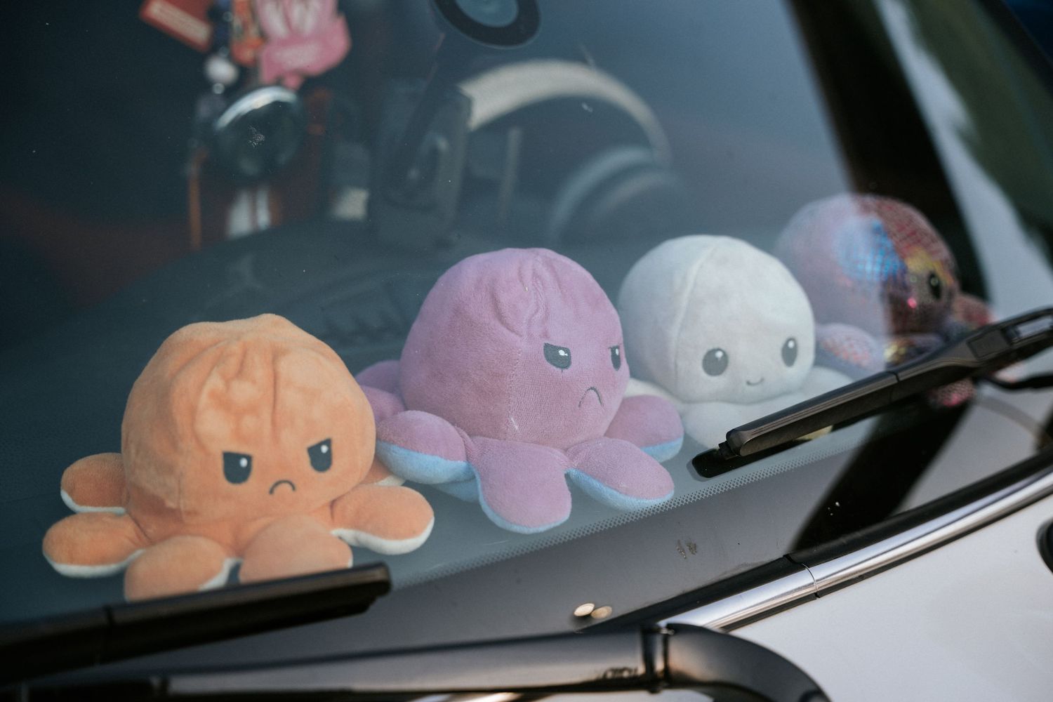 Three cute plush octopus toys displayed on a car's dashboard in orange, pink and white colors.