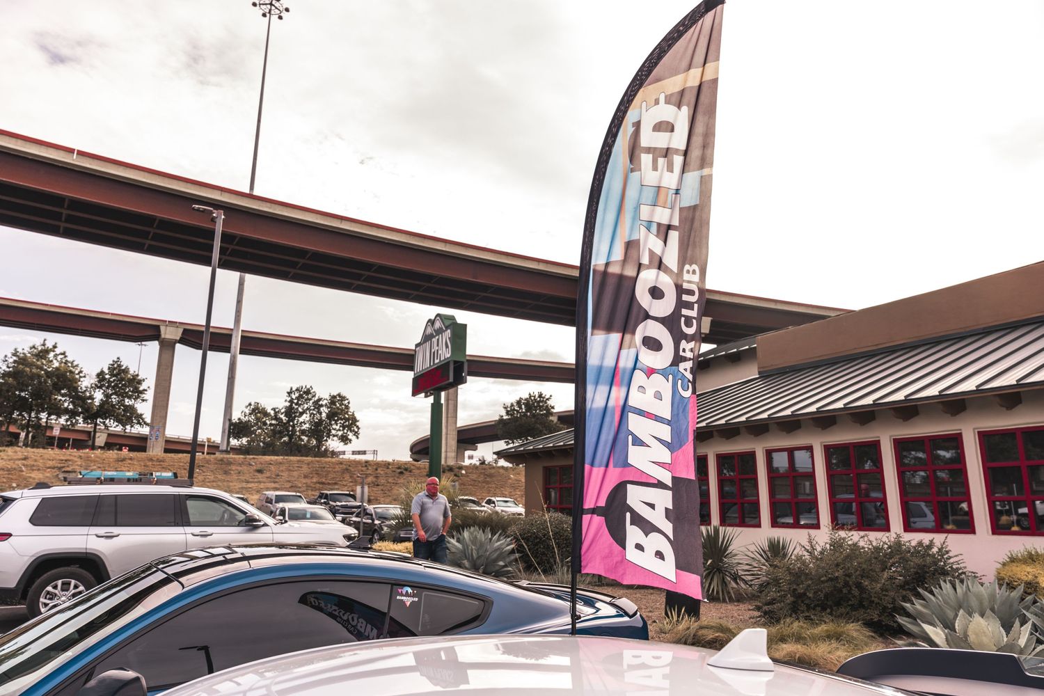 A tall banner flag stands in a parking lot with an overpass visible in the background.