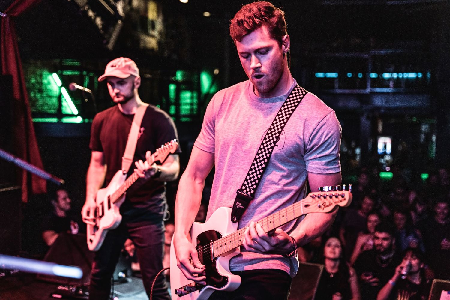 Musicians playing guitars perform under dramatic red stage lighting at club venue.