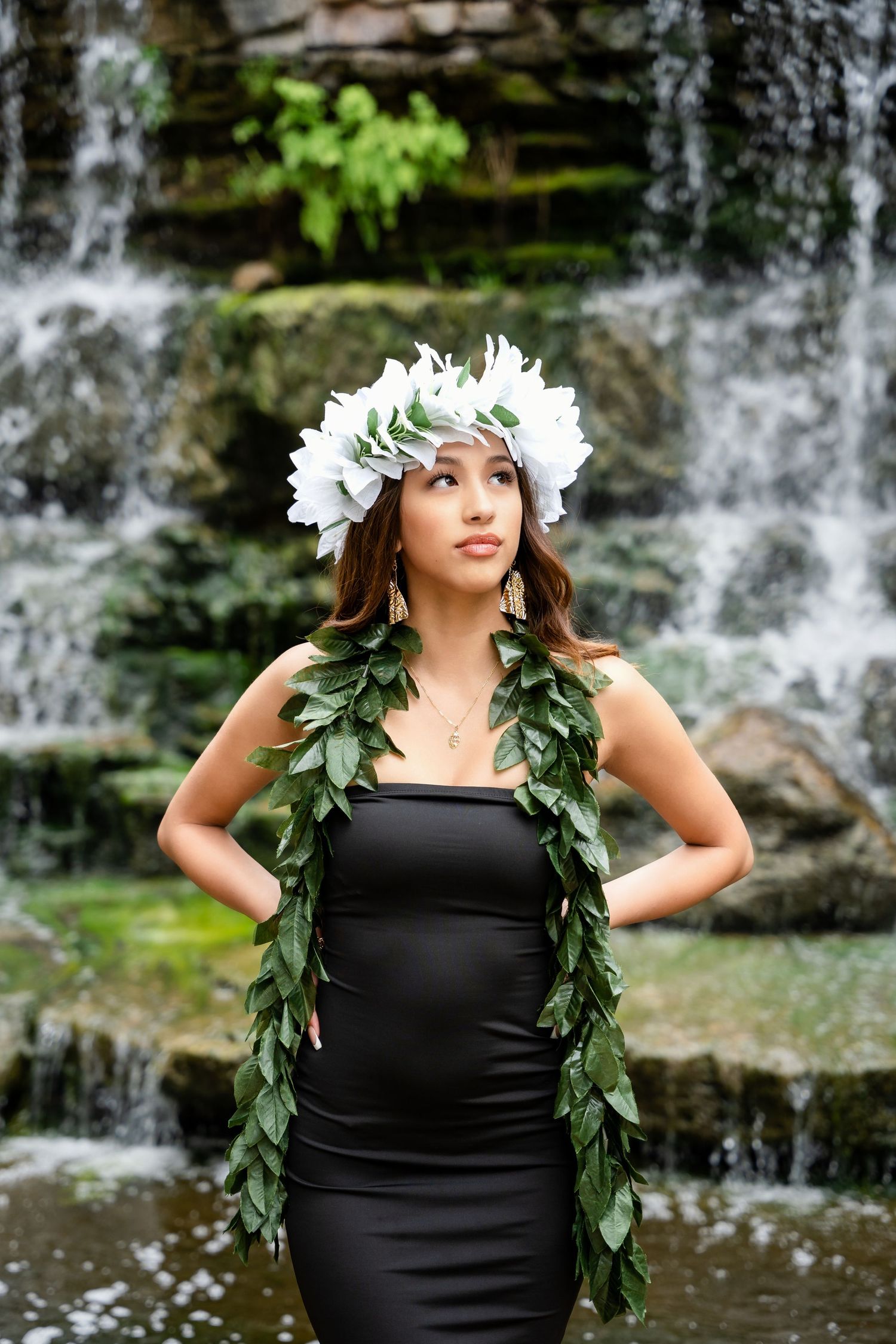 Elegant portrait with white floral headpiece and green leaf garland against cascading waterfall.