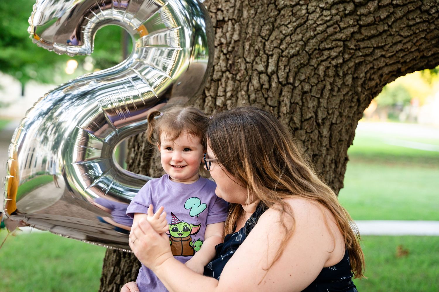 A cheerful outdoor moment with a silver number 2 balloon against a tree backdrop.