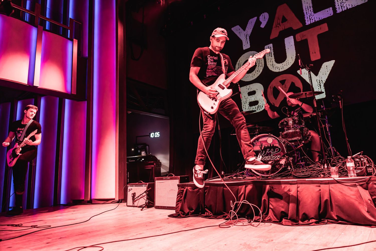 Bass player performs energetically on stage with dramatic lighting and 'Y'all Out Boy' signage visible.