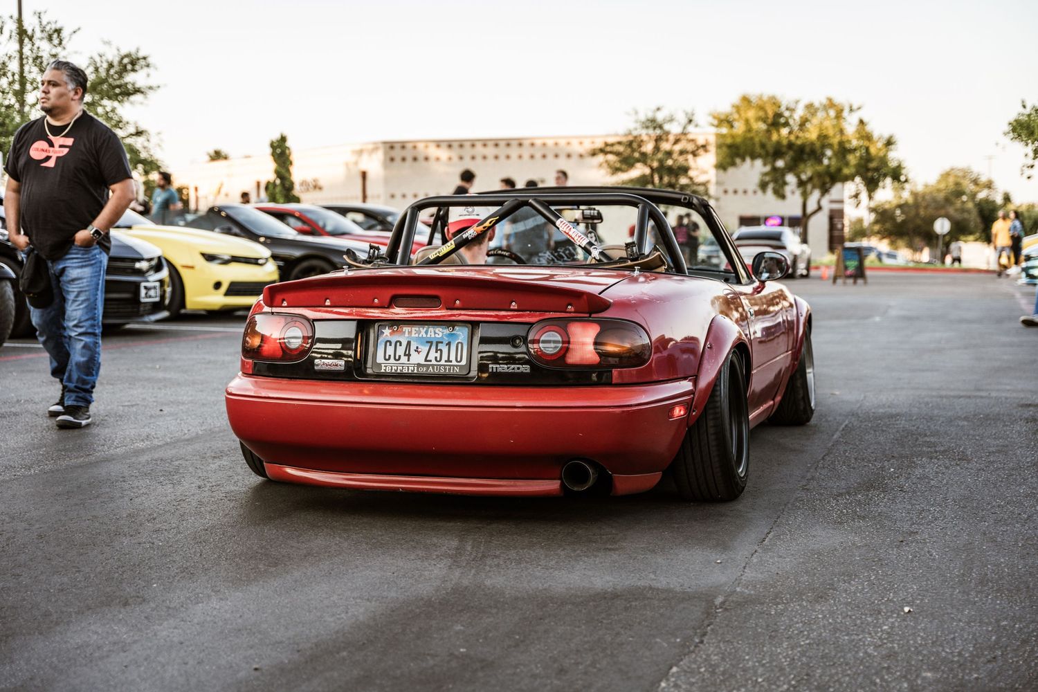 Red Mazda Miata convertible parked at outdoor car meet during sunset.