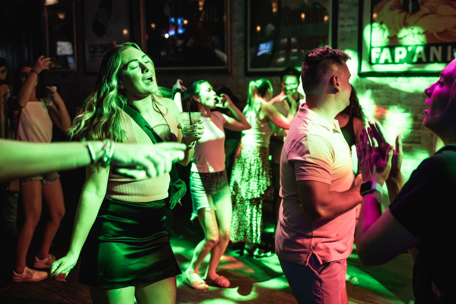 Crowd dances and celebrates at nightclub under colorful atmospheric lighting.