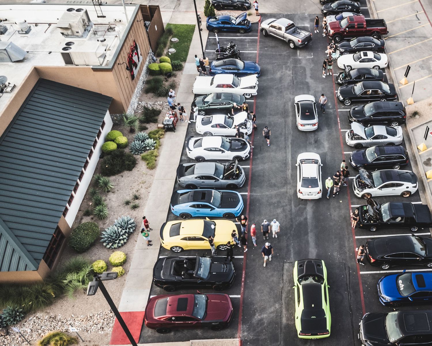 Overhead view of a parking lot car show with classic and modern vehicles lined up in rows.