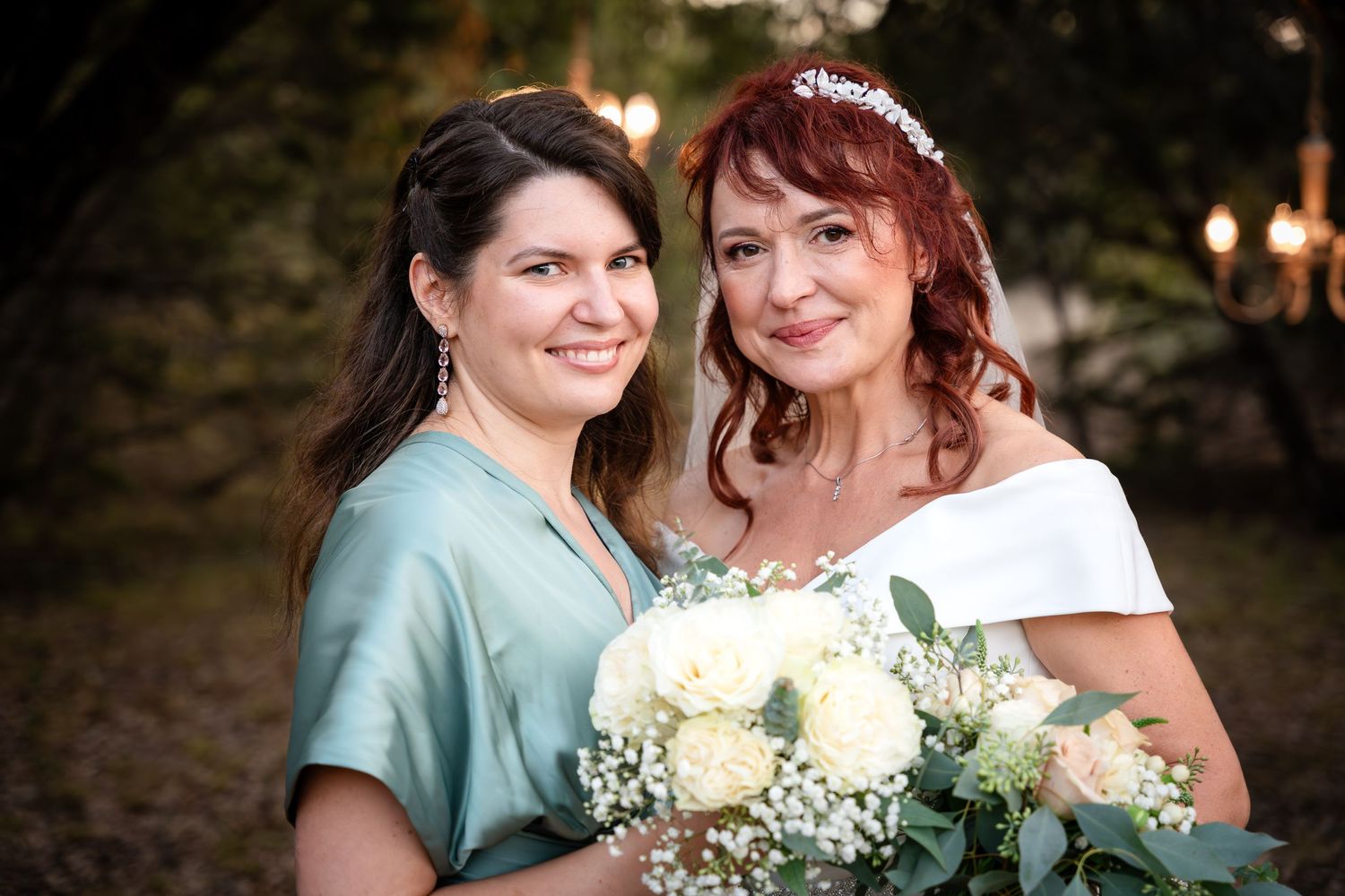 Two people pose together with a bouquet of white roses and baby's breath at an outdoor wedding.