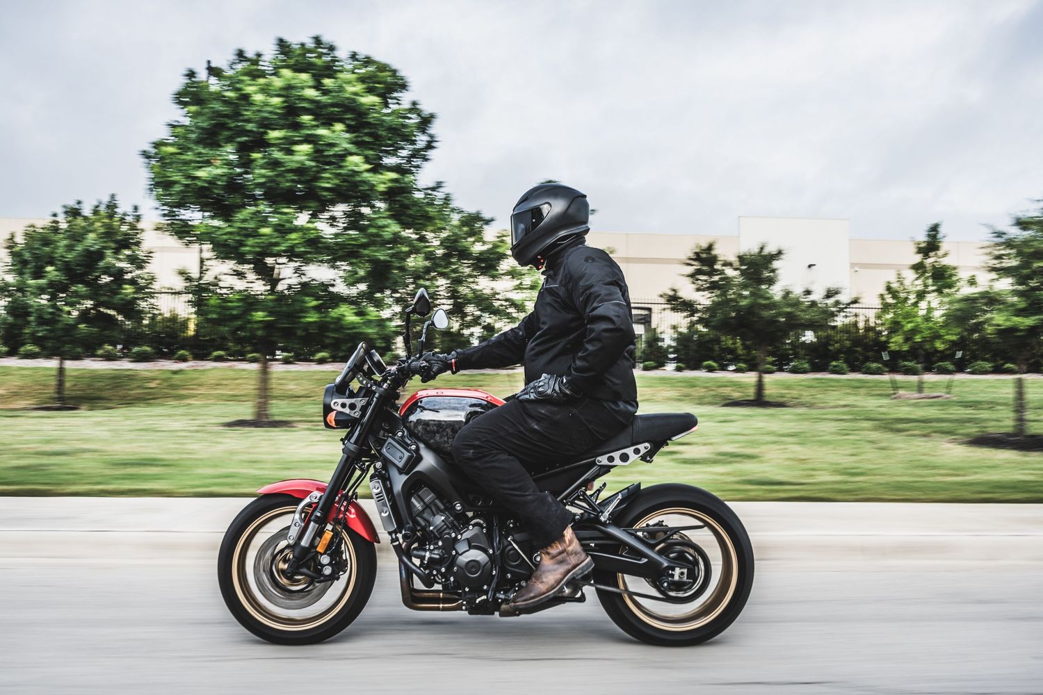Street bike rider in dark gear cruising past green suburban landscaping.