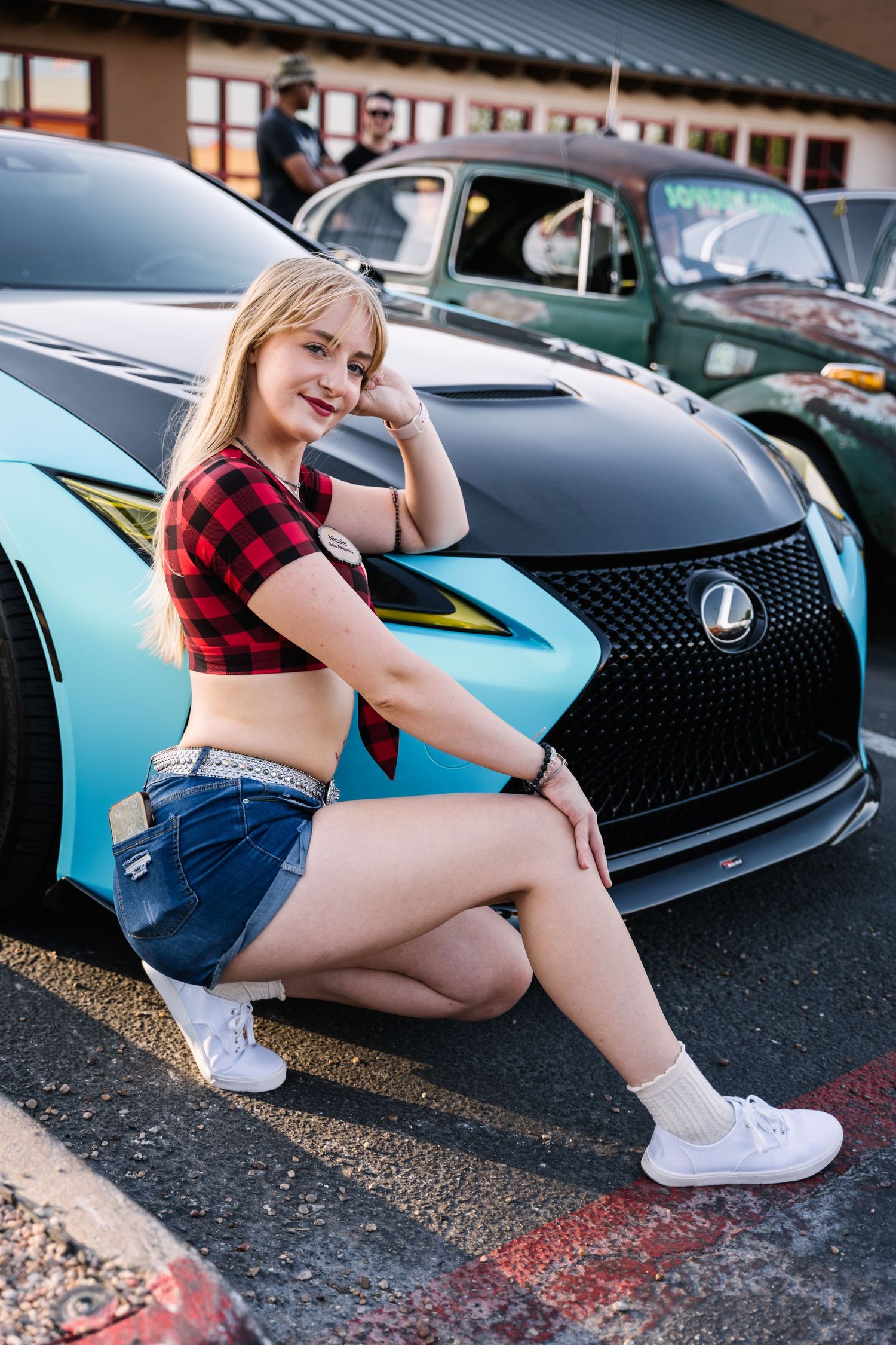 A model poses next to a blue and black Lexus sports car wearing casual attire.
