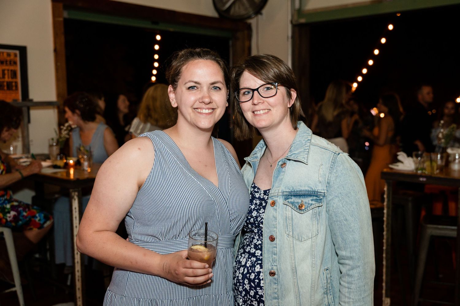Two friends share drinks and conversation at an evening social event.