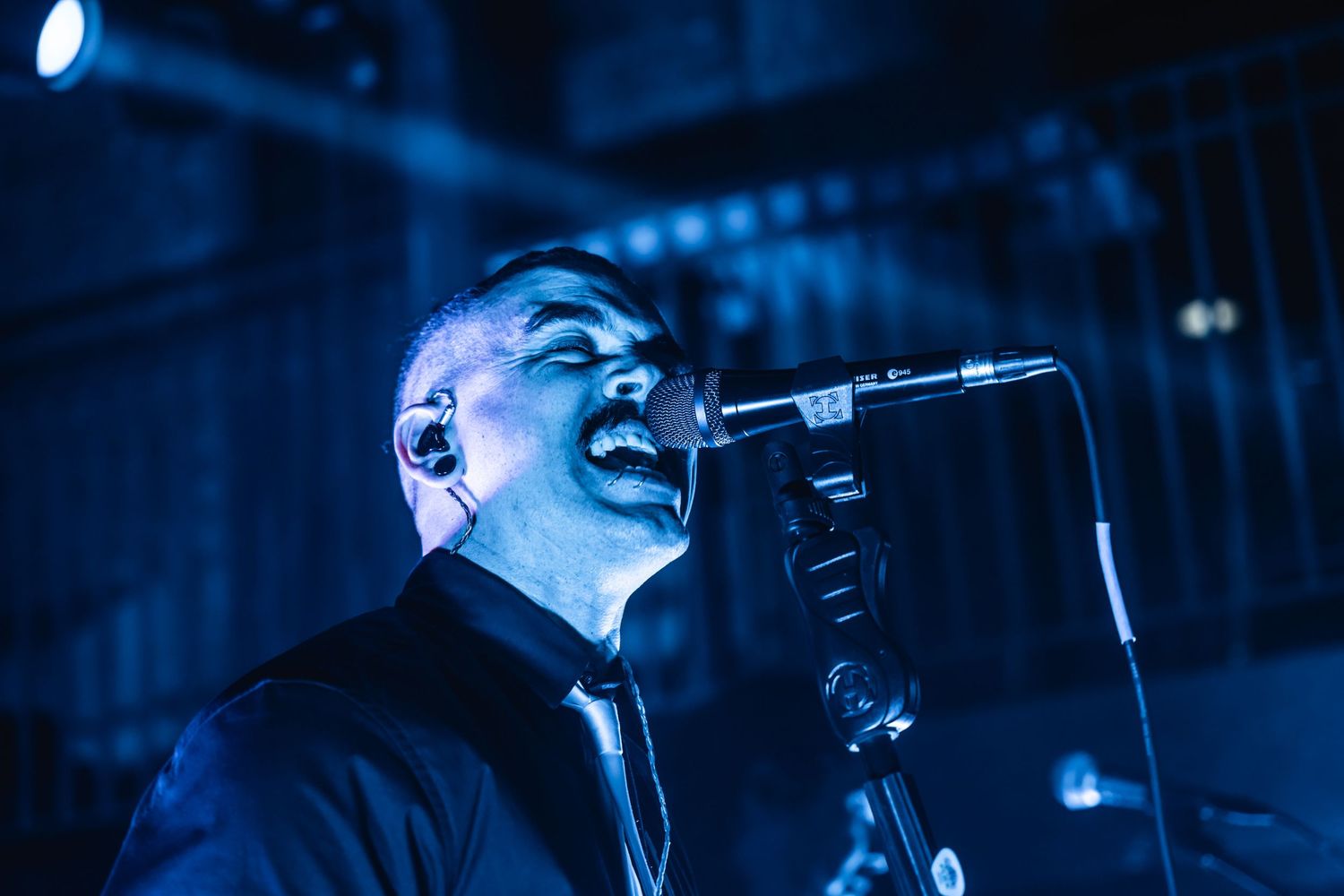 Concert performer singing passionately into microphone with blue stage lighting.