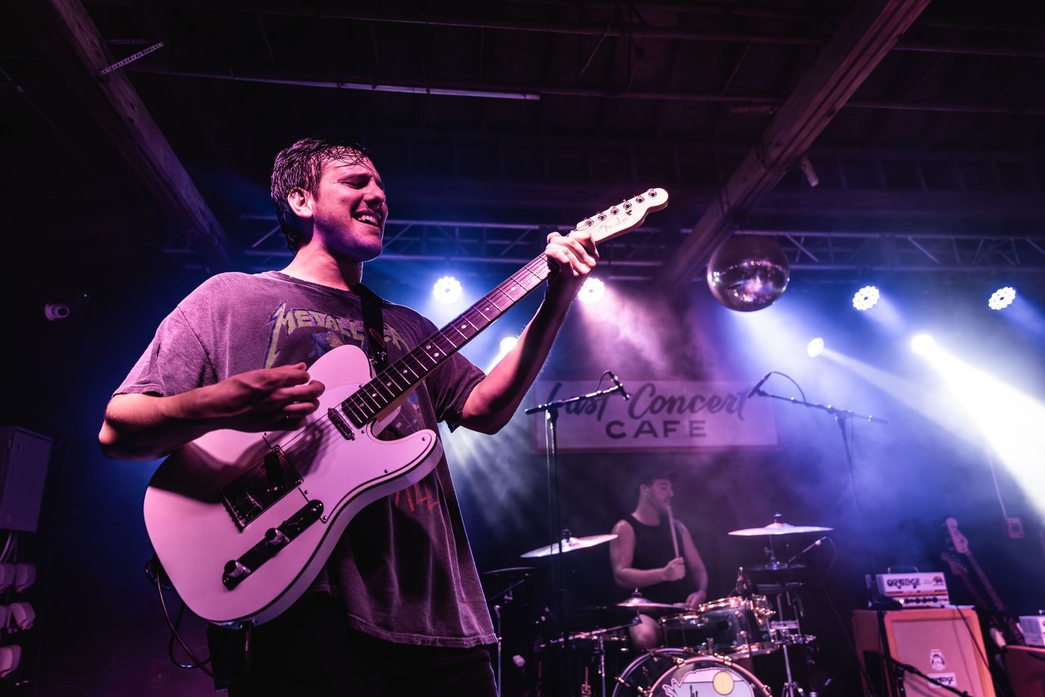 Guitarist plays electric guitar under blue stage lights at concert venue.