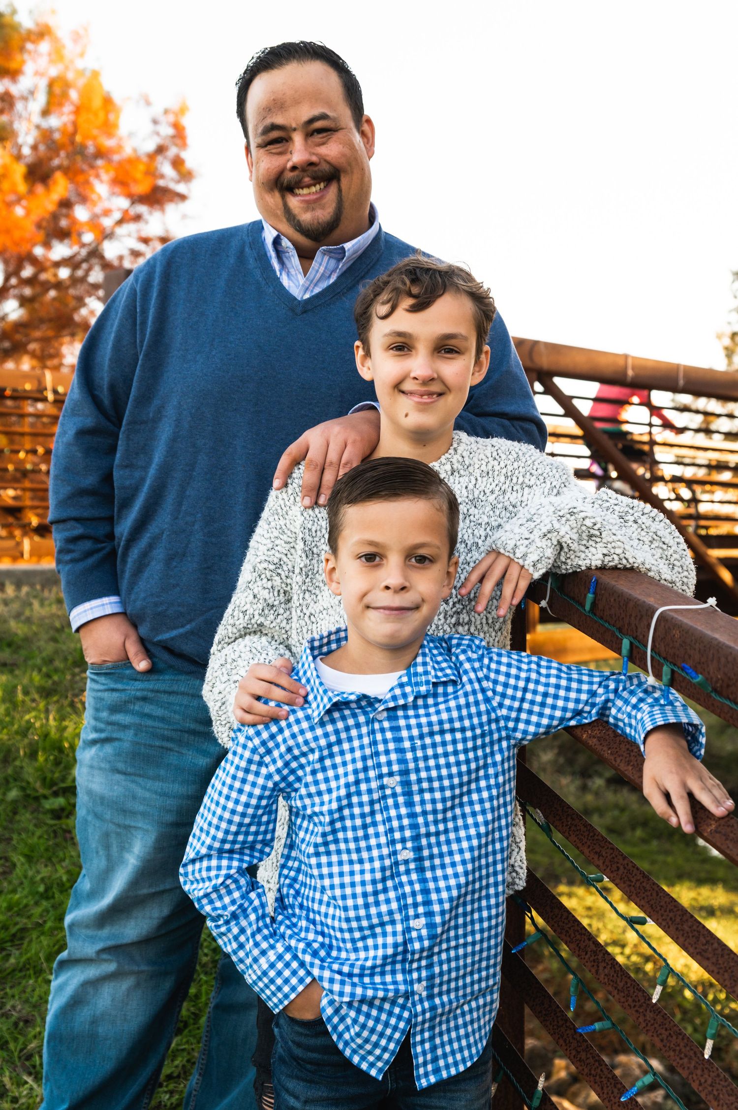Three people standing together outdoors with autumn foliage in background.