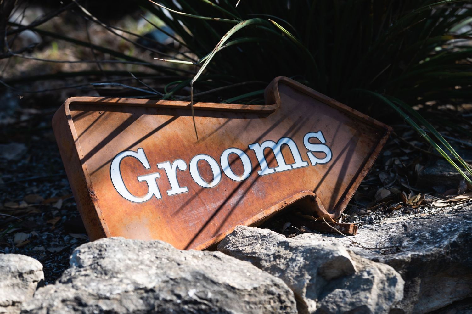 Wooden directional sign with 'Grooms' text displayed on rocky ground.