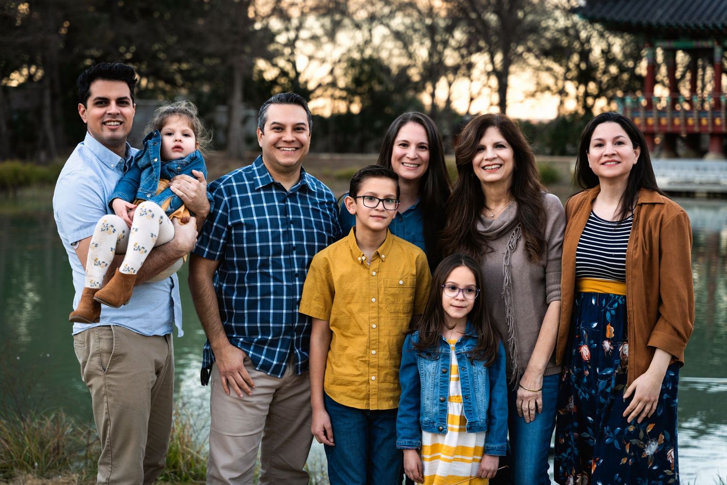 Multi-generational family group posing together outdoors at sunset near water.