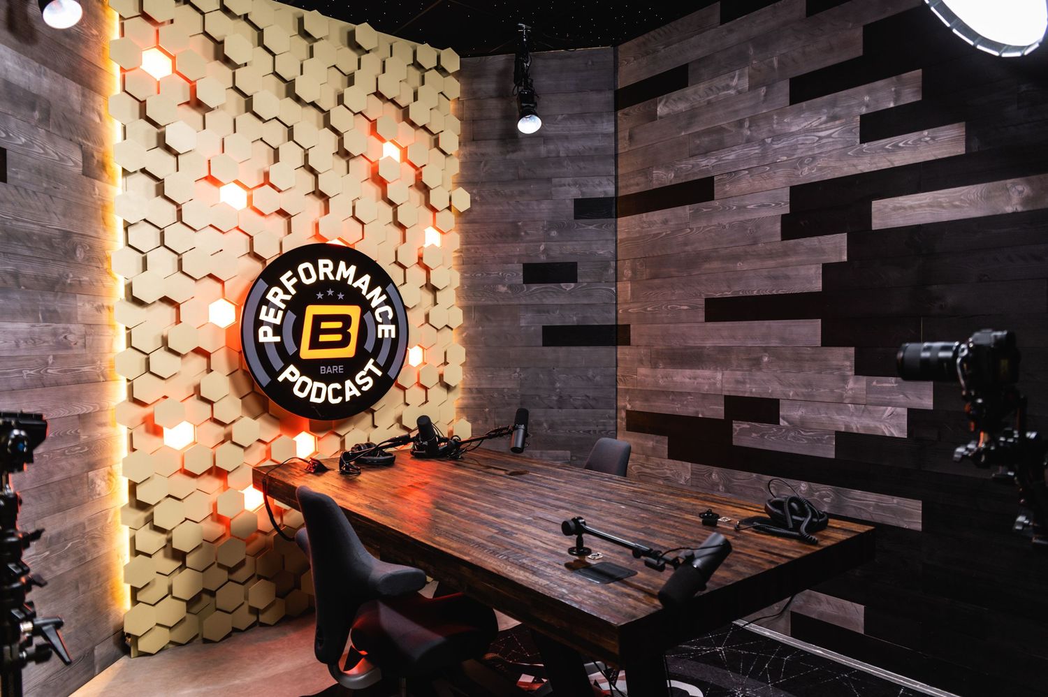 Stylish podcast studio setup with wooden table, microphones, and geometric wall design.