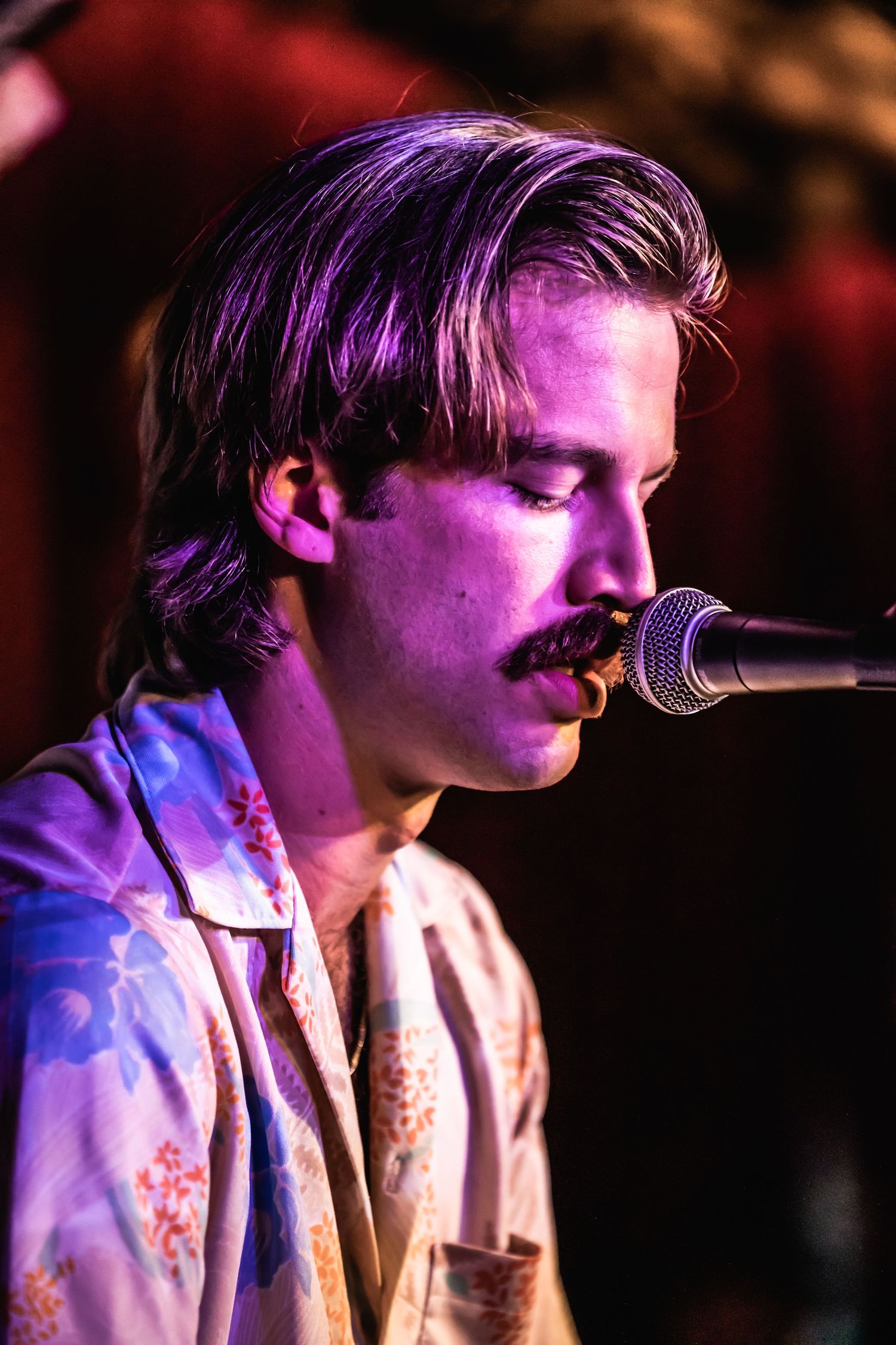 Close-up of musician singing into microphone under purple stage lighting.