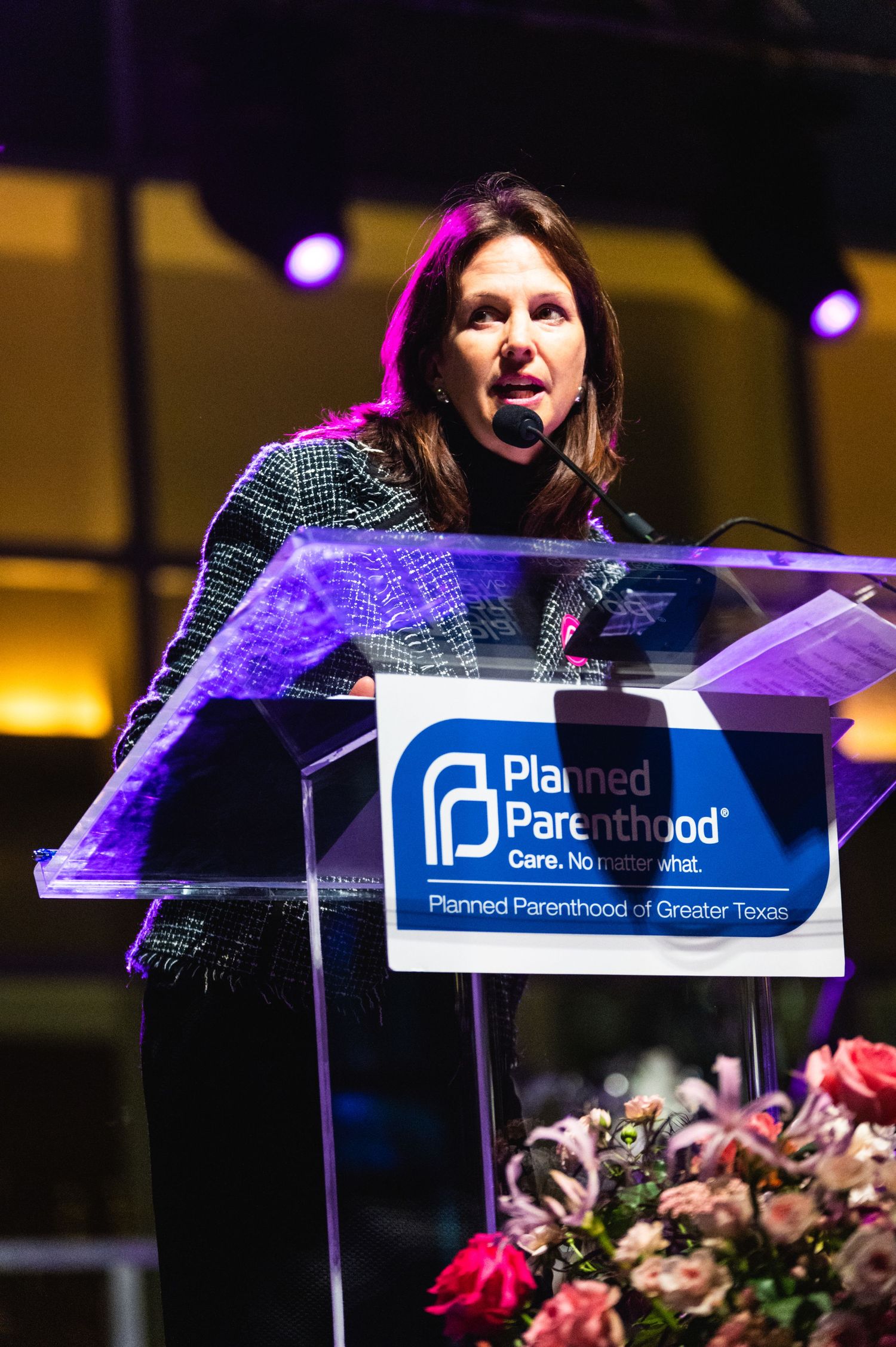 Speaker delivers remarks at Planned Parenthood podium with floral arrangements on stage.