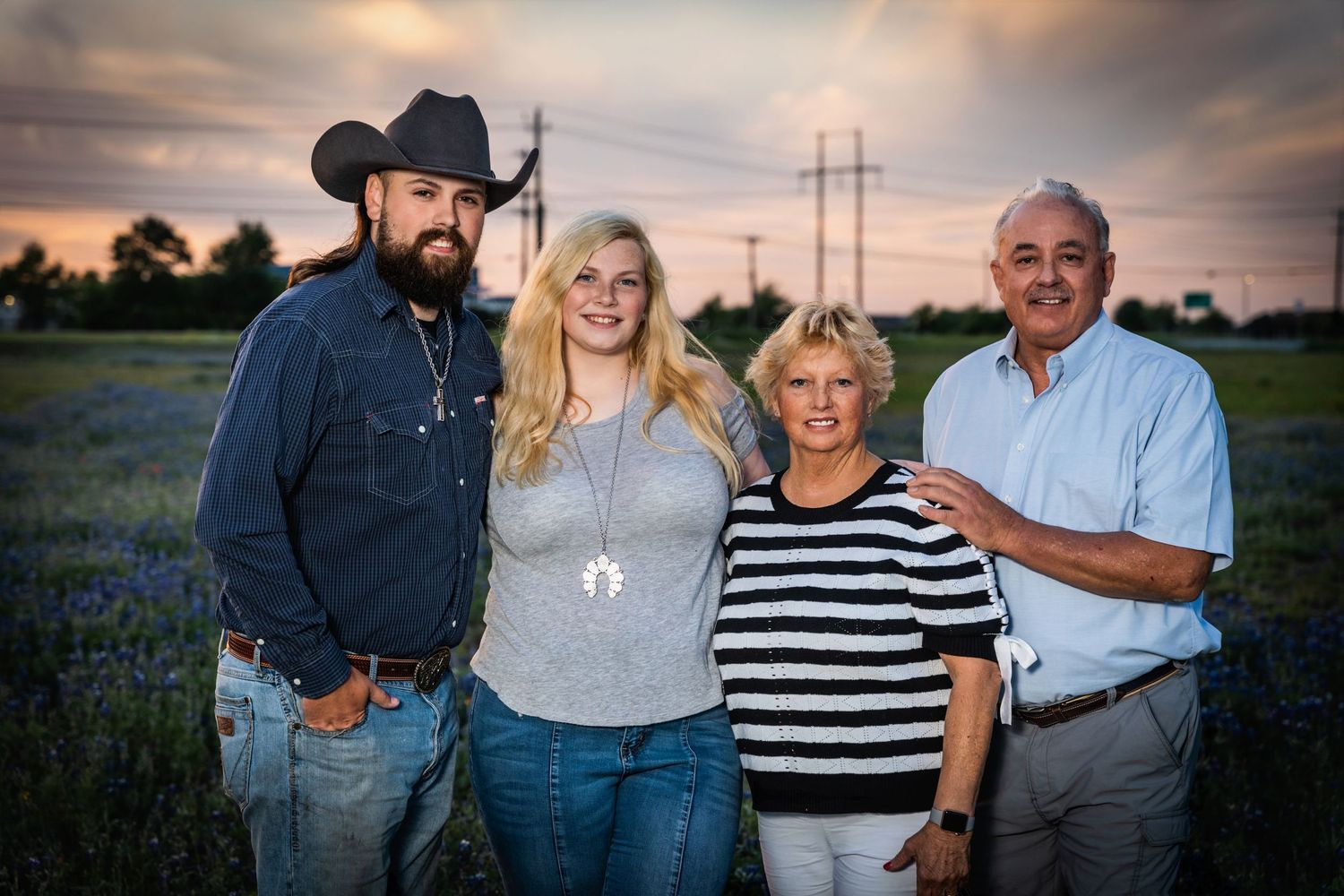 Family portrait in Texas bluebonnet field at sunset with power lines in background.