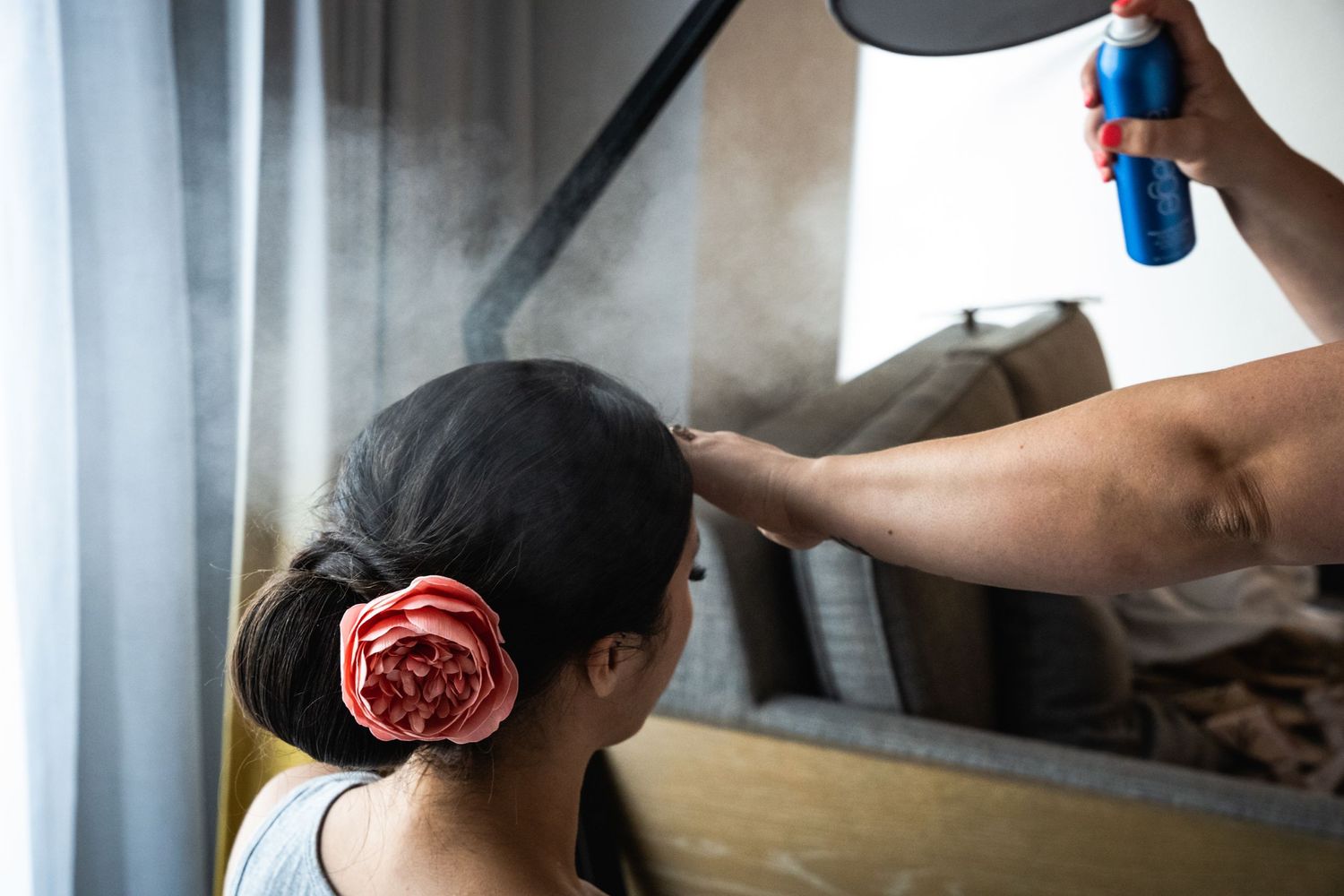 Hair stylist spraying product while styling a client's hair with a rose hair accessory.