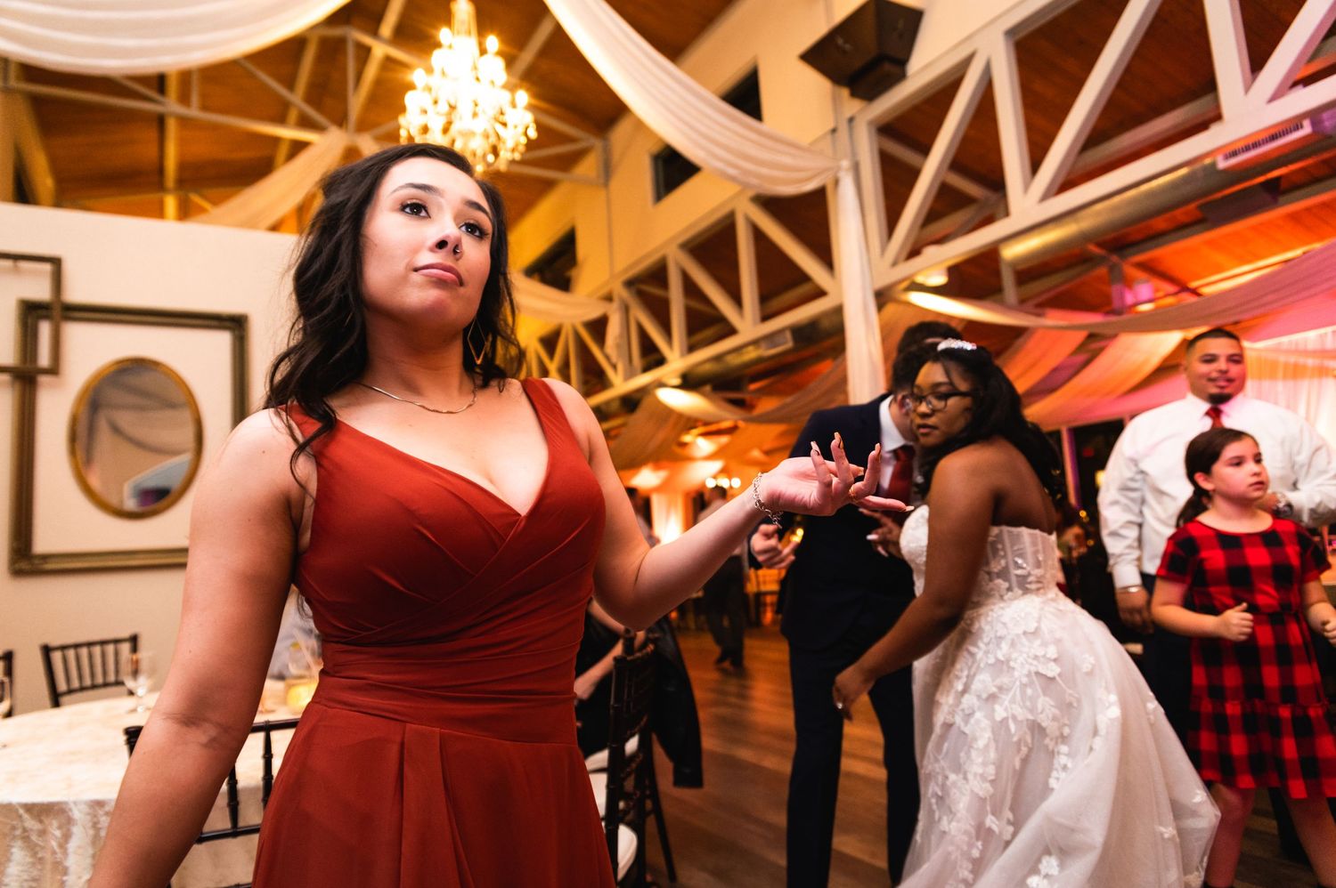Wedding guests dance and enjoy themselves at a reception under decorative ceiling beams.
