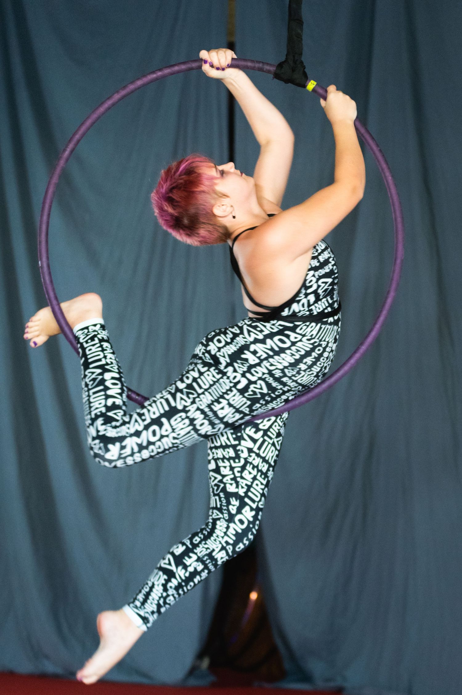 Aerial artist displays strength and flexibility while performing on purple lyra hoop.