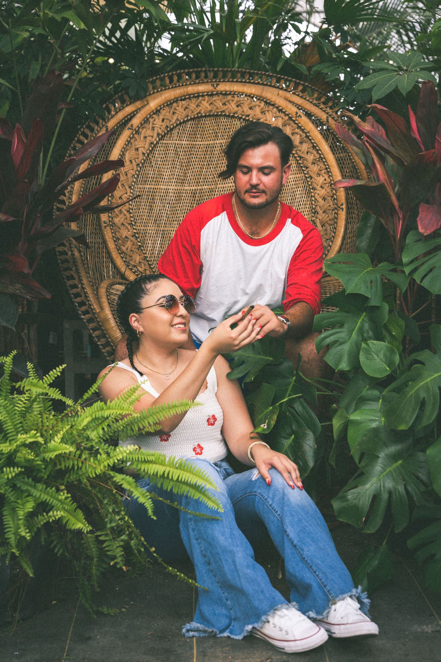 Couple sharing a playful moment in a tropical garden with peacock chair.