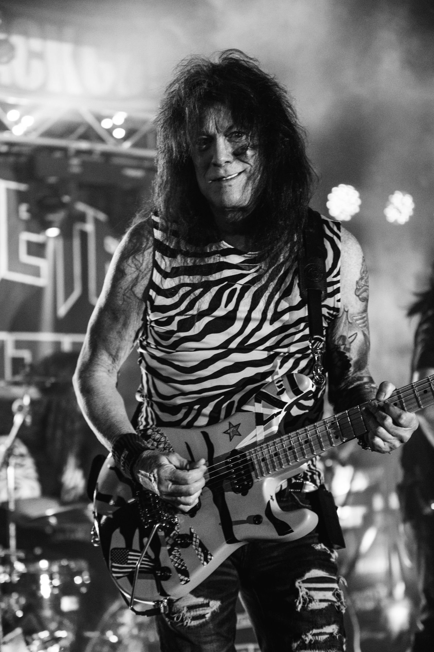 Guitar player in zebra print tank top performs energetically during rock concert.