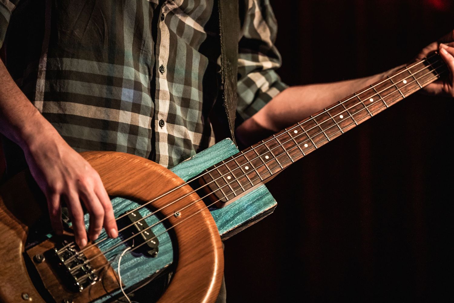 Detail shot of hands playing a resonator guitar with turquoise details.