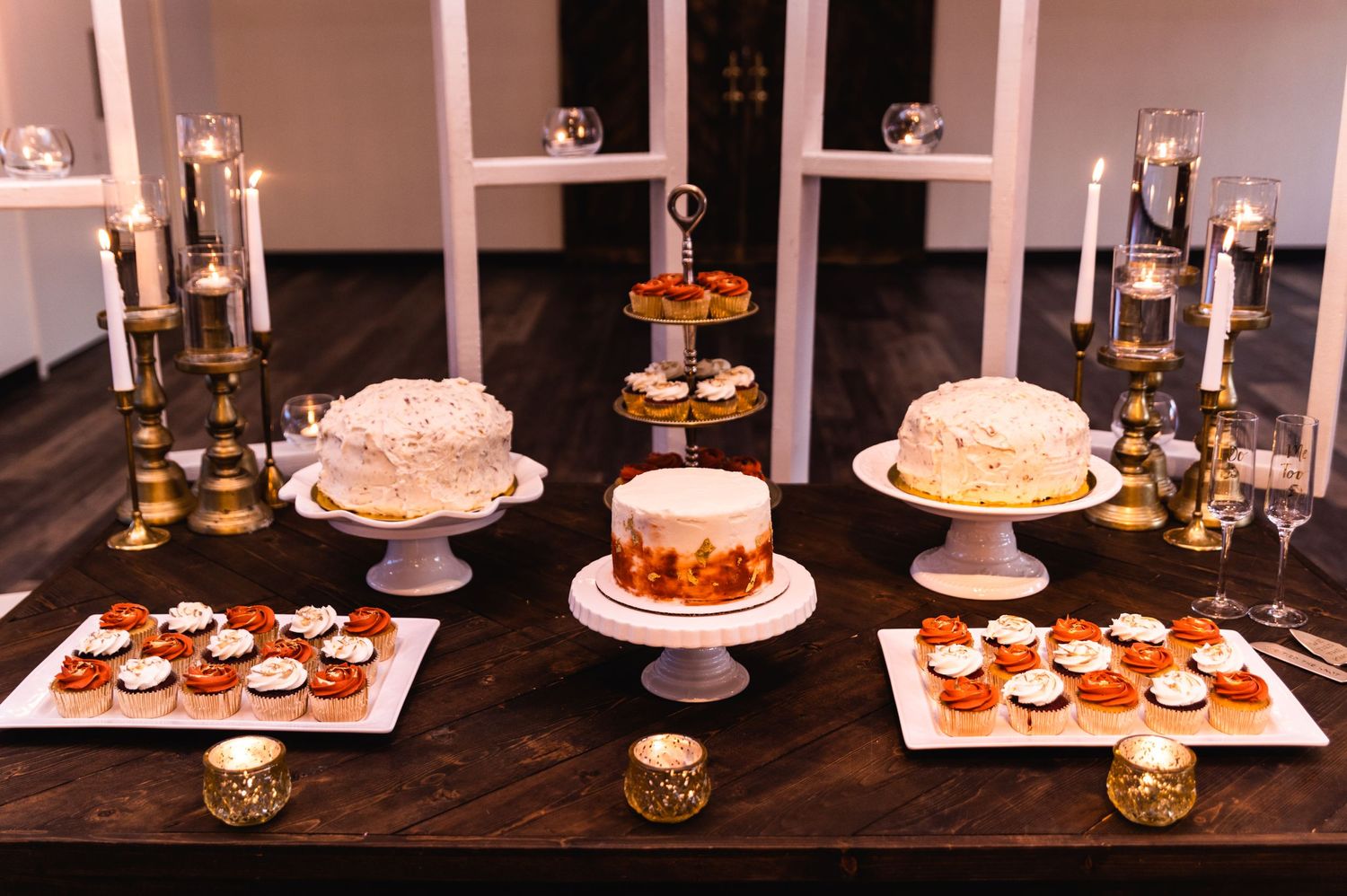 Elegant wedding dessert table with tiered cakes, cupcakes, and candlelit decor.